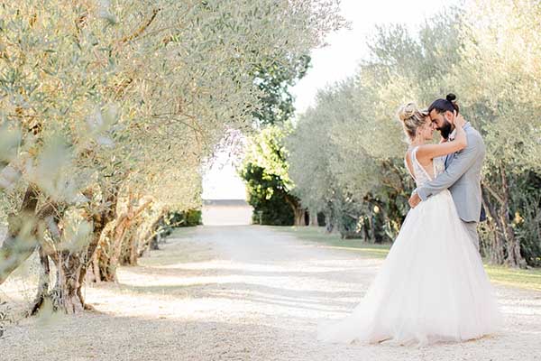 Photo d'un couple de marié qui pose pour une photo dans une allée bordée d'oliviers en Provence
