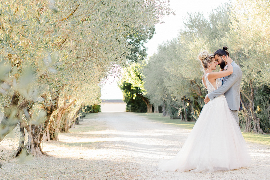 Photo d'un couple de marié qui se promène dans une allée bordée d'oliviers à Marseille