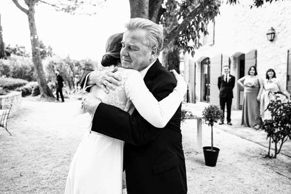 Photographie en noir et blanc d'une étreinte entre la mariée et son père.