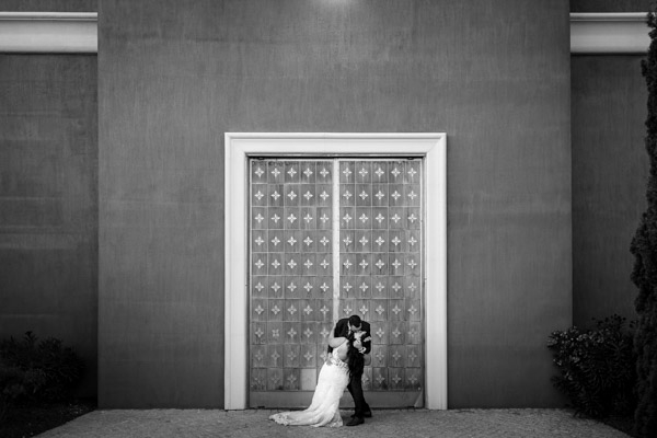 Photo artistique en noir et blanc d'un baiser devant une porte monumentale.