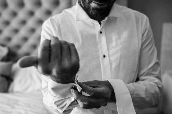 Détail en noir et blanc du marié fermant ses boutons de manchette.