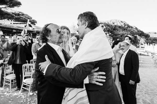 Émotion et accolade entre deux hommes lors d'une cérémonie de mariage sur la plage.