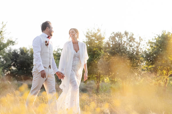 Mariés marchant main dans la main dans un champ doré à l'heure dorée en Provence.