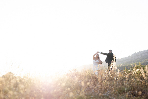 Silhouette lointaine d'un couple de mariés dansant dans un champ au coucher du soleil.