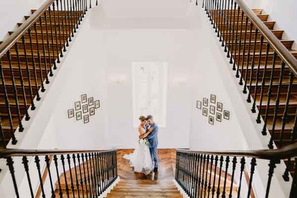 Vue en plongée d'un couple de mariés s'enlaçant au pied d'un grand escalier symétrique.