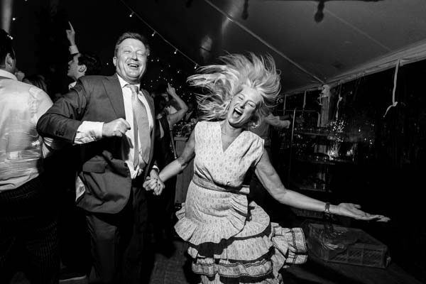 Photo dynamique en noir et blanc d'un couple d'invités dansant avec enthousiasme lors d'une soirée de mariage.