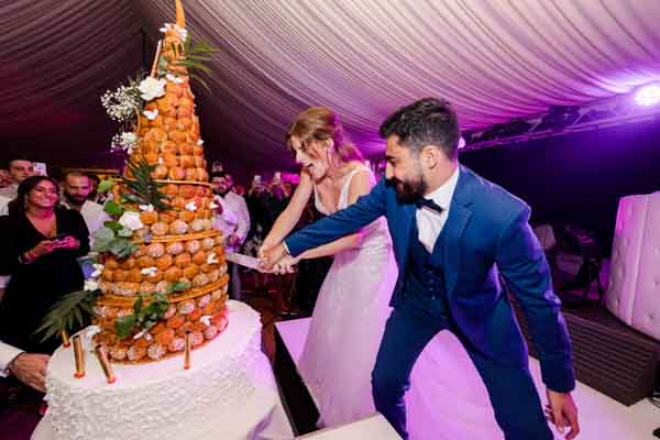Les mariés coupant ensemble une pièce montée de choux traditionnelle sous des lumières festives.