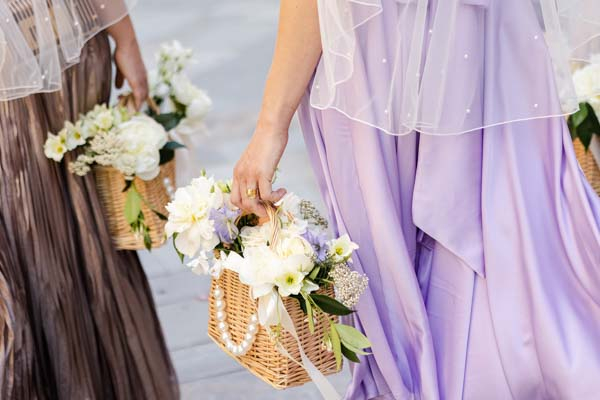 Détail des demoiselles d'honneur portant des paniers en osier garnis de fleurs blanches et perles.