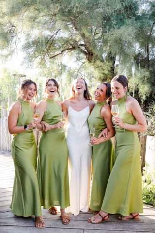 Groupe de demoiselles d'honneur en robes vertes riant avec la mariée en extérieur.