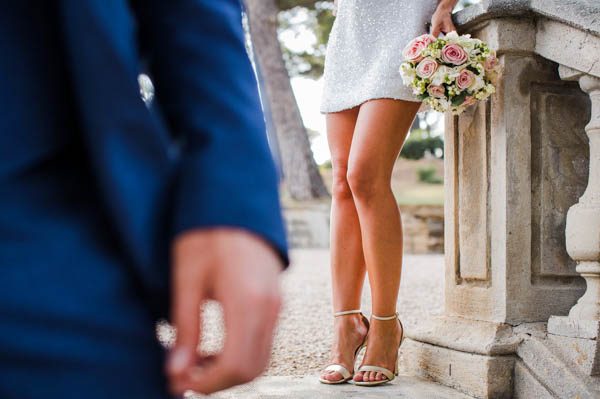 Mariée en robe courte tenant son bouquet, focus sur les chaussures dorées à bride.