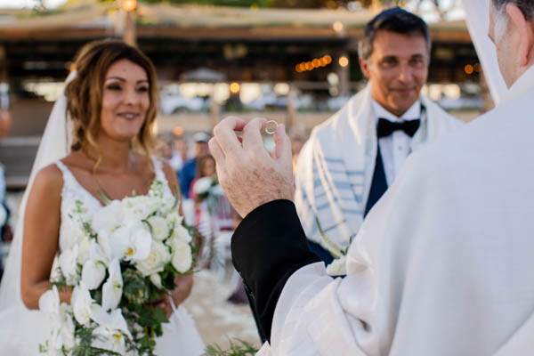 Gros plan sur l'échange des alliances lors d'une cérémonie de mariage en extérieur sous la houppa.