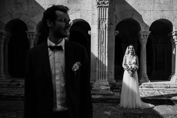 Portrait artistique en noir et blanc d'une mariée sous les arches d'un cloître en Provence.
