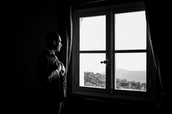 Silhouette d'un marié ajustant sa cravate devant une fenêtre lumineuse en noir et blanc.