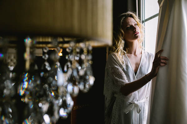 Portrait d'une mariée pensive près d'une fenêtre derrière un lustre en cristal.