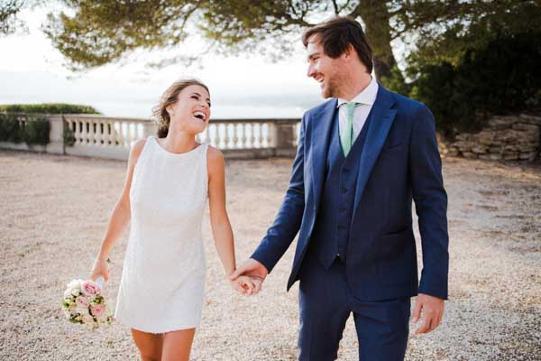 Mariée en robe courte riant avec son époux en extérieur.