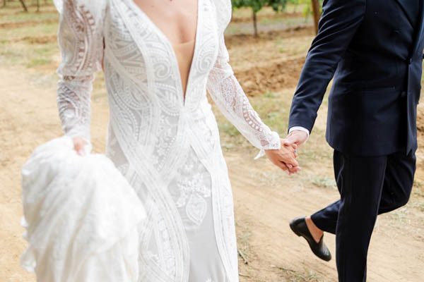 Couple de mariés marchant main dans la main dans un domaine viticole en Provence.