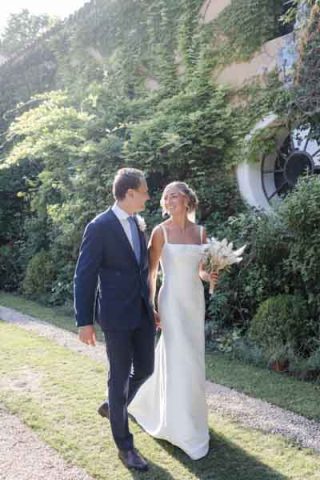 Couple de mariés marchant main dans la main dans un jardin méditerranéen.