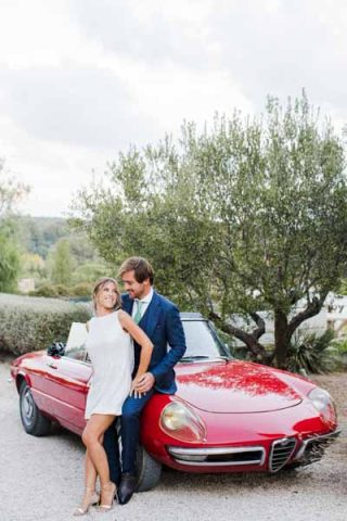 Couple de mariés posant sur une Alfa Romeo rouge vintage en Provence.