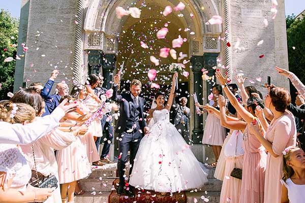 Sortie d'église des mariés sous une pluie de pétales roses et blancs lors d'une cérémonie religieuse à Aix-en-Provence.