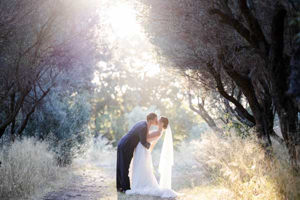Couple de mariés s'embrassant sur un chemin d'oliviers, soleil couchant, ambiance romantique en Provence.