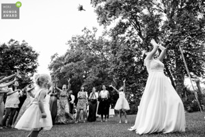 Photo de mariage primée en noir et blanc montrant une mariée lançant son bouquet à un groupe d'invitées enthousiastes en extérieur.