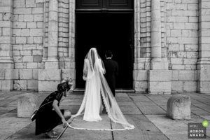Photographie de mariage primée en noir et blanc montrant une mariée de dos avec un long voile entrant dans une église historique en Provence.
