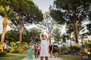 Photographie de mariage primée montrant une invitée en robe claire attrapant le bouquet de fleurs lancé par la mariée dans un parc en Provence.
