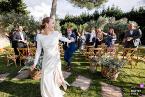 Photographie de mariage primée montrant une mariée radieuse courant et riant avec ses invités lors d'une cérémonie en extérieur en Provence.
