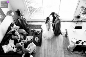Photographie de mariage primée en noir et blanc montrant une mariée entourée de ses amies lors des préparatifs dans un salon lumineux.