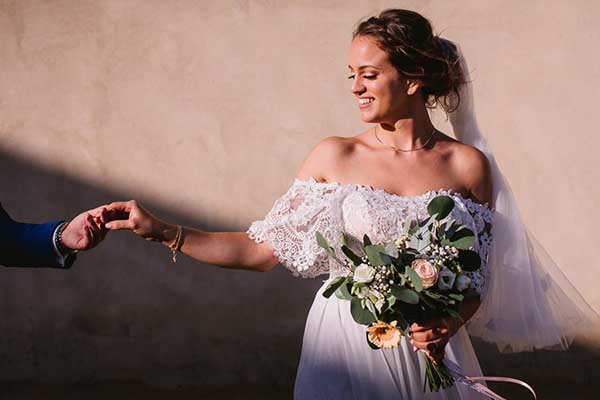 Portrait lumineux d'une mariée souriante portant une robe en dentelle et un bouquet de fleurs champêtres en Provence.