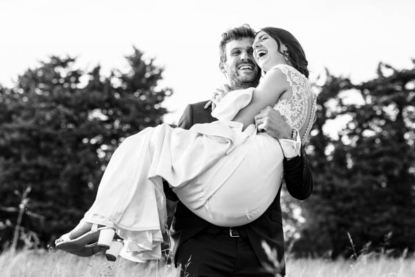 Marié portant sa femme dans un champ en noir et blanc.