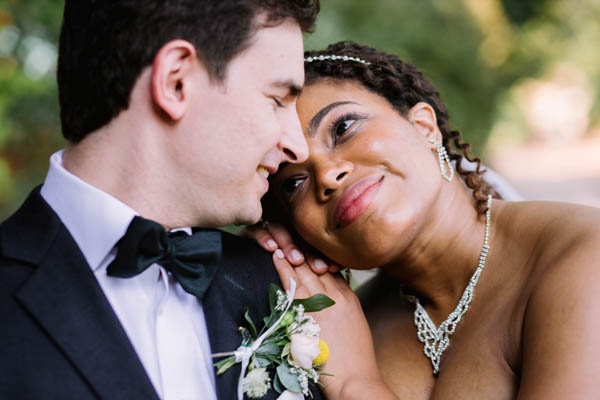 Portrait serré d'un couple de mariés partageant un regard tendre et souriant en extérieur.