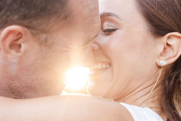 Portrait serré et lumineux d'un couple de mariés s'embrassant à contre-jour dans le soleil couchant.