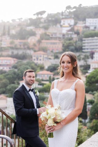 Mariée souriante avec son bouquet devant un paysage de la Côte d'Azur.