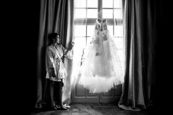 Mariée en peignoir de soie admirant sa robe de mariée suspendue devant une fenêtre lumineuse dans un mas en Provence.