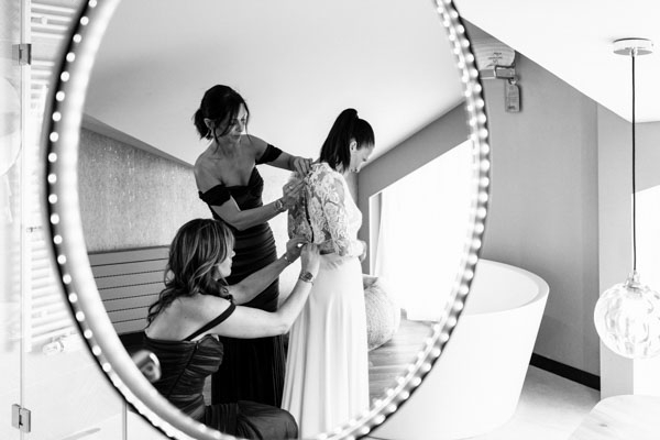 Reflet dans un miroir de deux femmes aidant la mariée à ajuster sa robe de mariée.