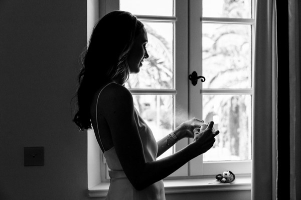 Profil en ombre chinoise d'une mariée vaporisant son parfum devant une fenêtre en Provence.