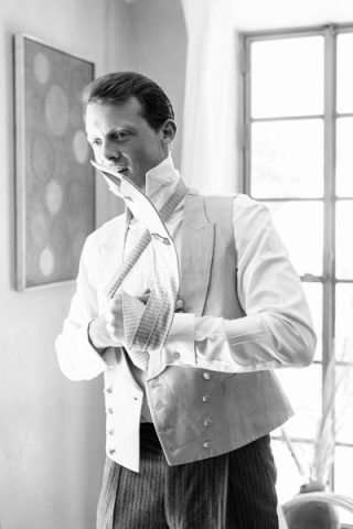 Portrait en noir et blanc du marié ajustant sa cravate et son gilet avant la cérémonie.