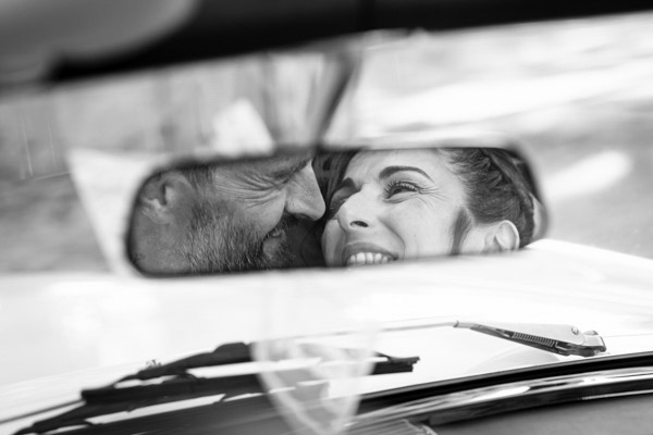 Reflet dans le rétroviseur d'un couple de mariés complices dans une voiture de collection.