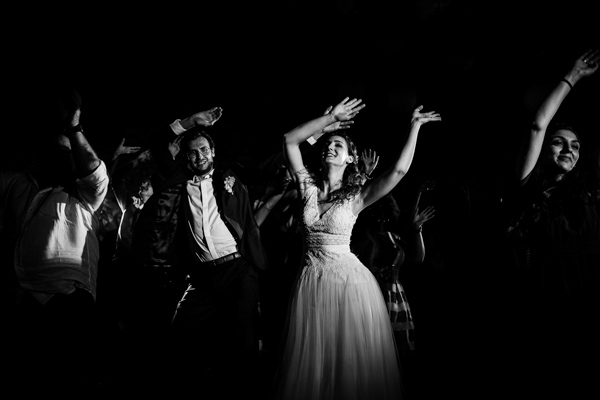 Photographie de mariage en noir et blanc des mariés dansant avec leurs invités en soirée.