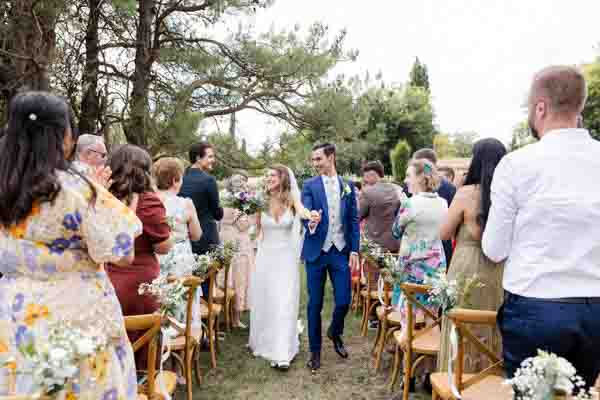 Mariés tout sourire remontant l'allée sous les applaudissements des invités lors d'une cérémonie en extérieur.
