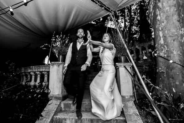 Couple de mariés descendant les marches en levant les mains, célébration en noir et blanc.