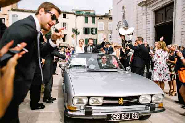 Mariés saluant la foule dans une Peugeot 504 cabriolet grise.