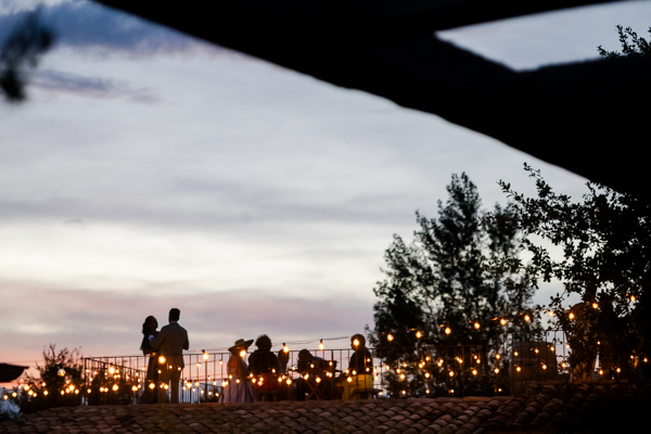 Silhouette d'invités profitant du coucher de soleil sur la terrasse du Domaine de Brès, avec des guirlandes guinguette allumées.