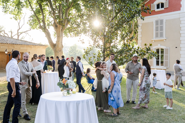 Invités discutant et célébrant lors du vin d'honneur ensoleillé dans les jardins du Château de Vergières.