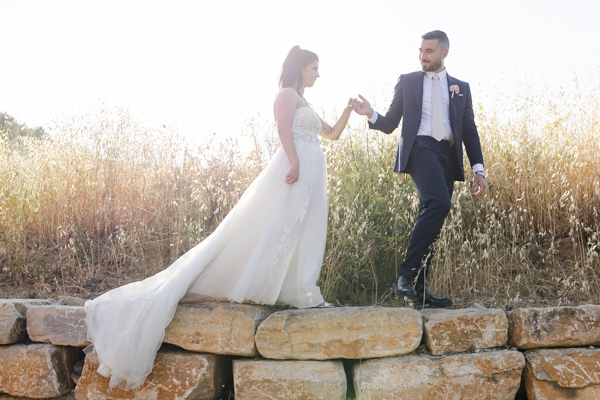 Couple de mariés se tenant la main sur un muret en pierre au Domaine Bunan, séance photo romantique à la lumière dorée du soir.