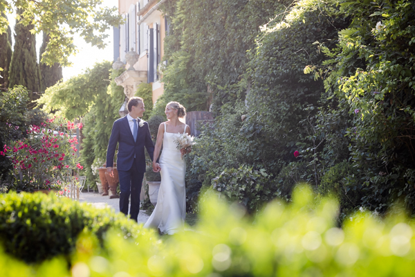 Couple de mariés se tenant la main et marchant dans les jardins fleuris de la Bastide du Régent après leur cérémonie.