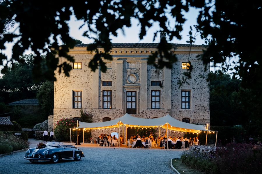 Vue de nuit du dîner de mariage sous une tente nomade illuminée, devant la façade éclairée du Château de Vaugrenier.