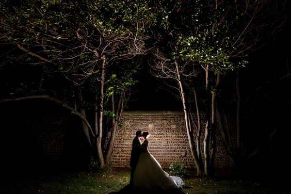 Photo de couple de mariage créative de nuit, silhouette des mariés devant un mur en pierre éclairé dans le parc du Château de Vergières.