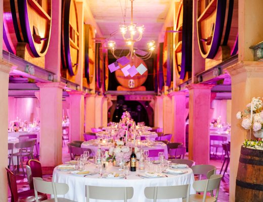 Salle de réception de mariage installée dans le chai du Domaine Bunan, éclairée en rose, avec les grands foudres en arrière-plan.